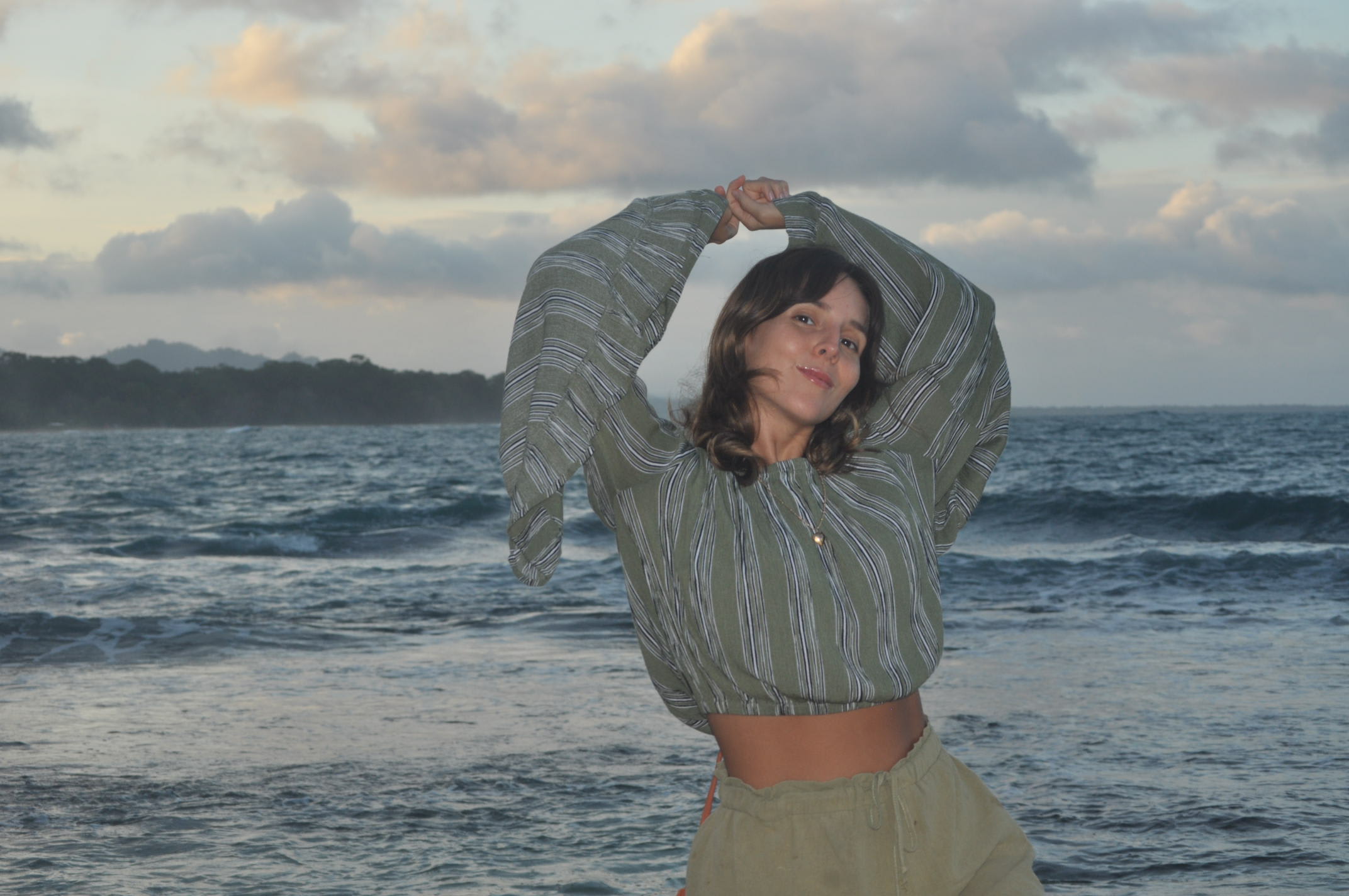 Luz smiling at the camera with her hands together above her head and ocean waves in the background