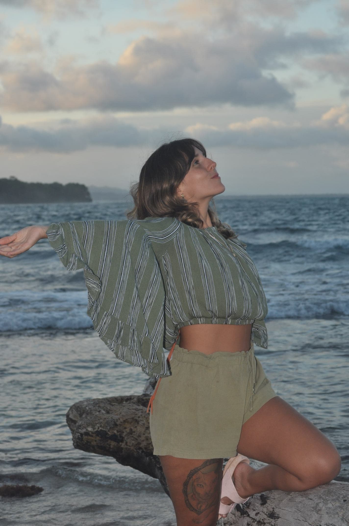 Luz with her arms open toward the sky and the ocean behind her
