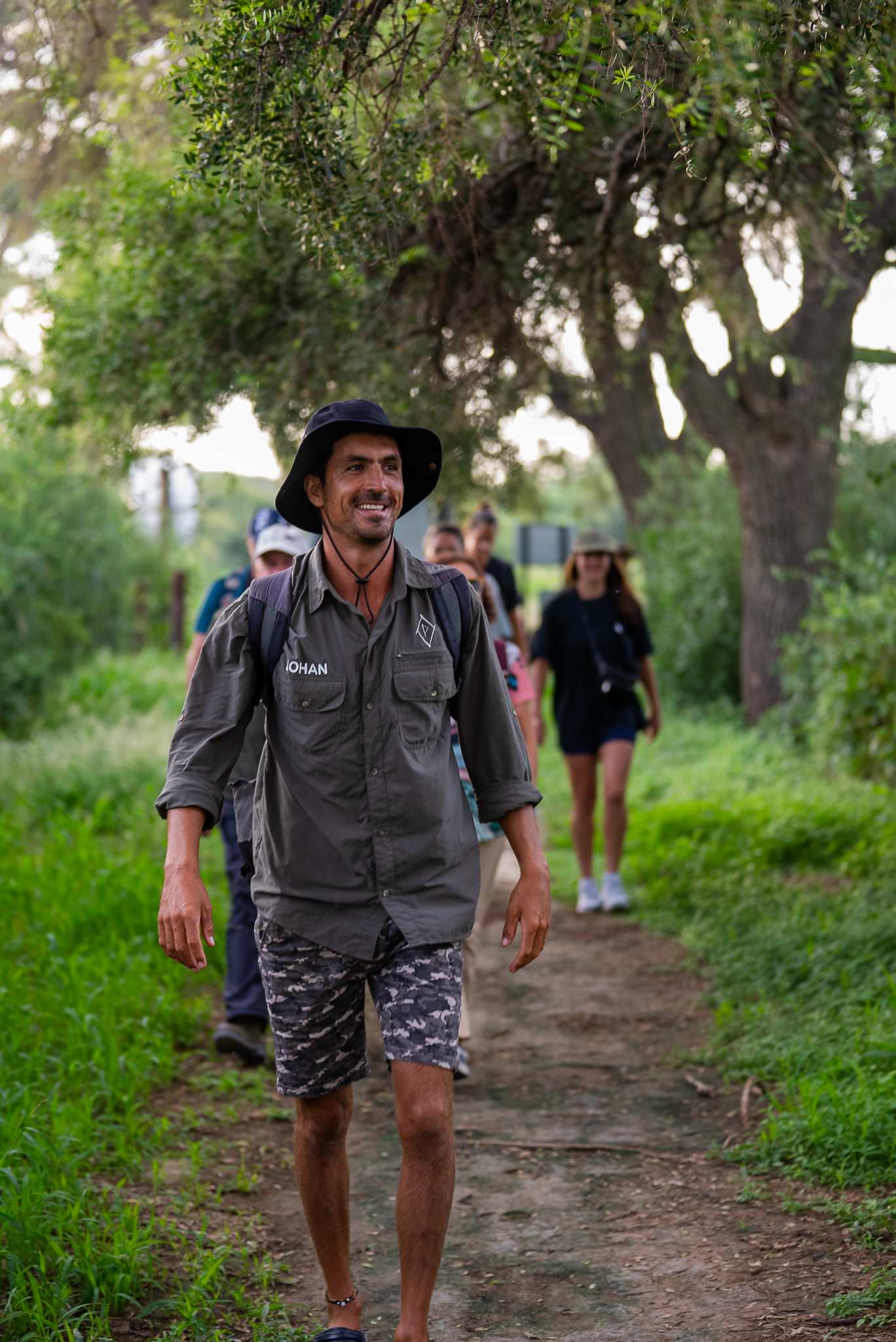 Biólogo caminando y sornriendo en primer plano con turistas en un sendero