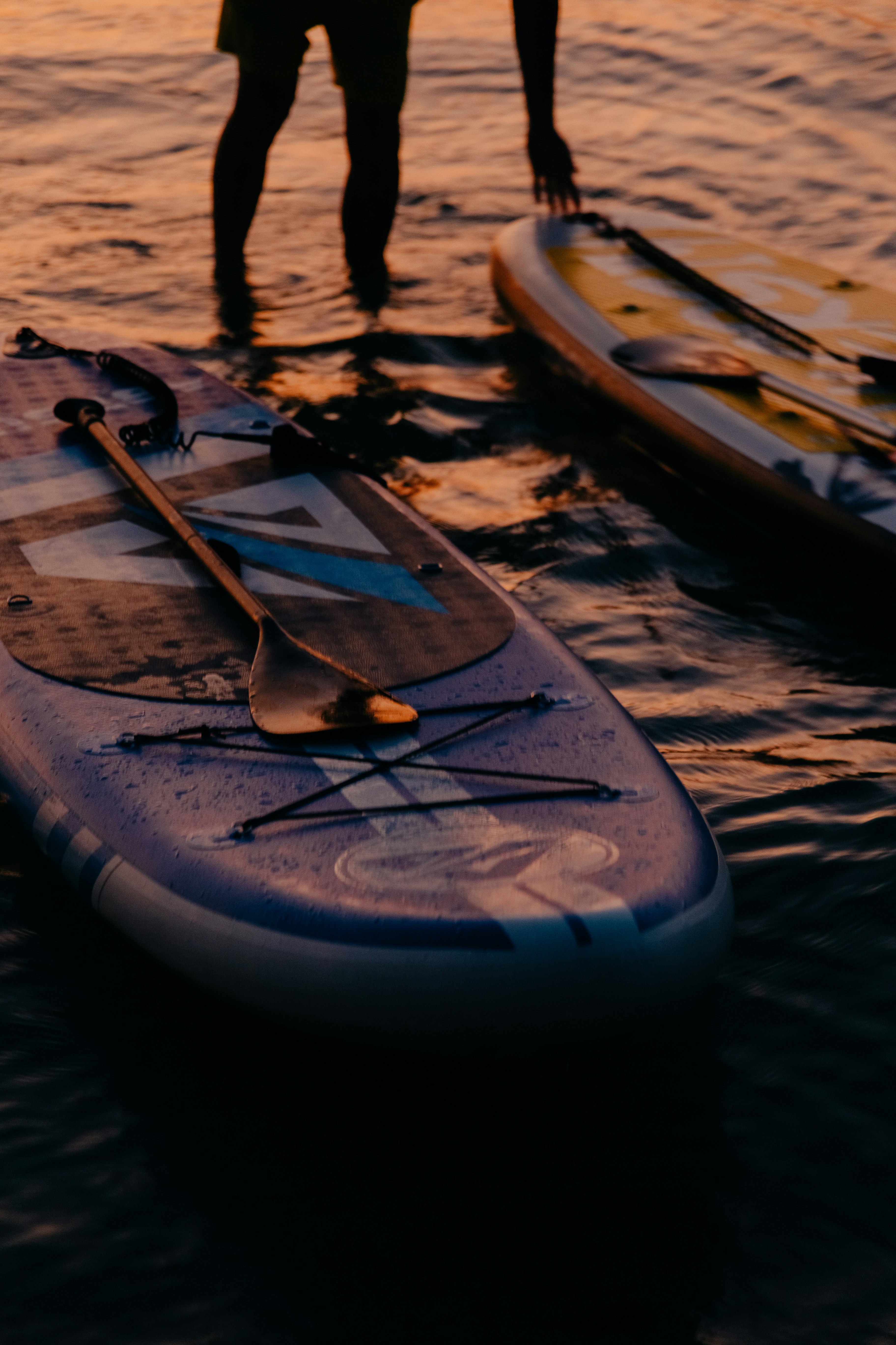 Tabla de Paddle board en el agua con el reflejo del atardecer encima.