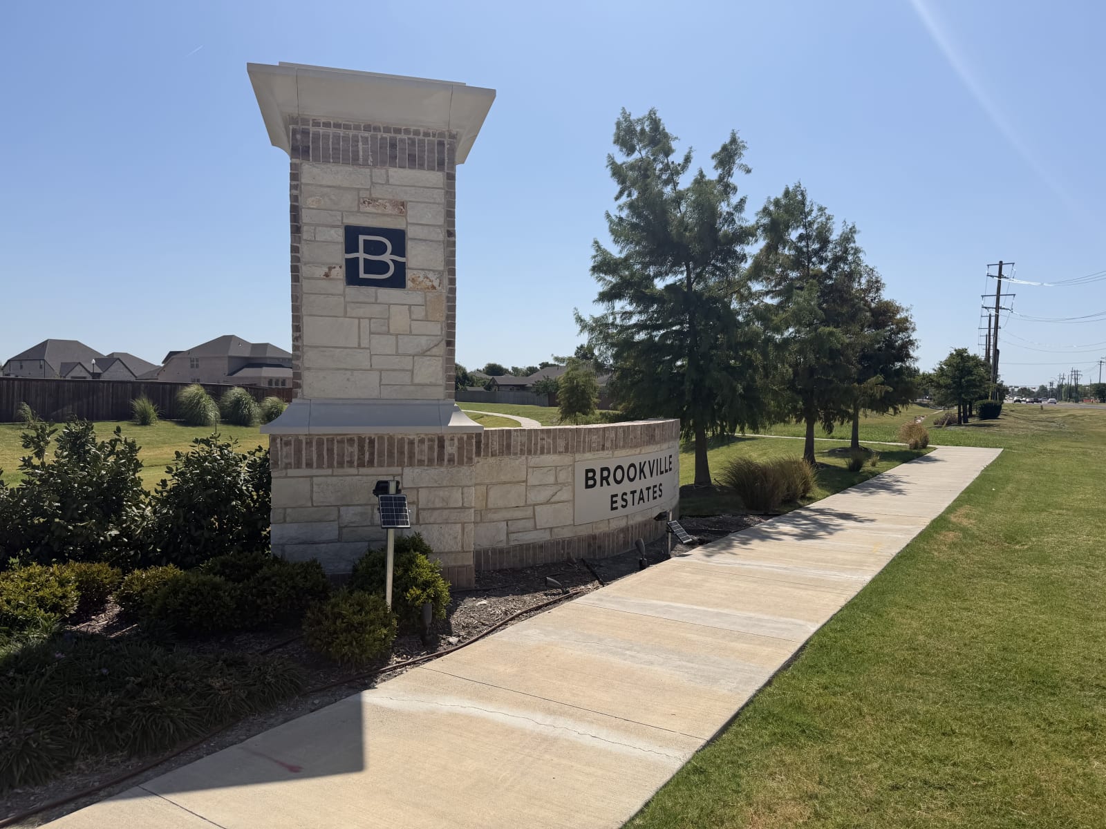 Brookville Estates stone entry column and monument wall beside a concrete sidewalk in Forney, TX