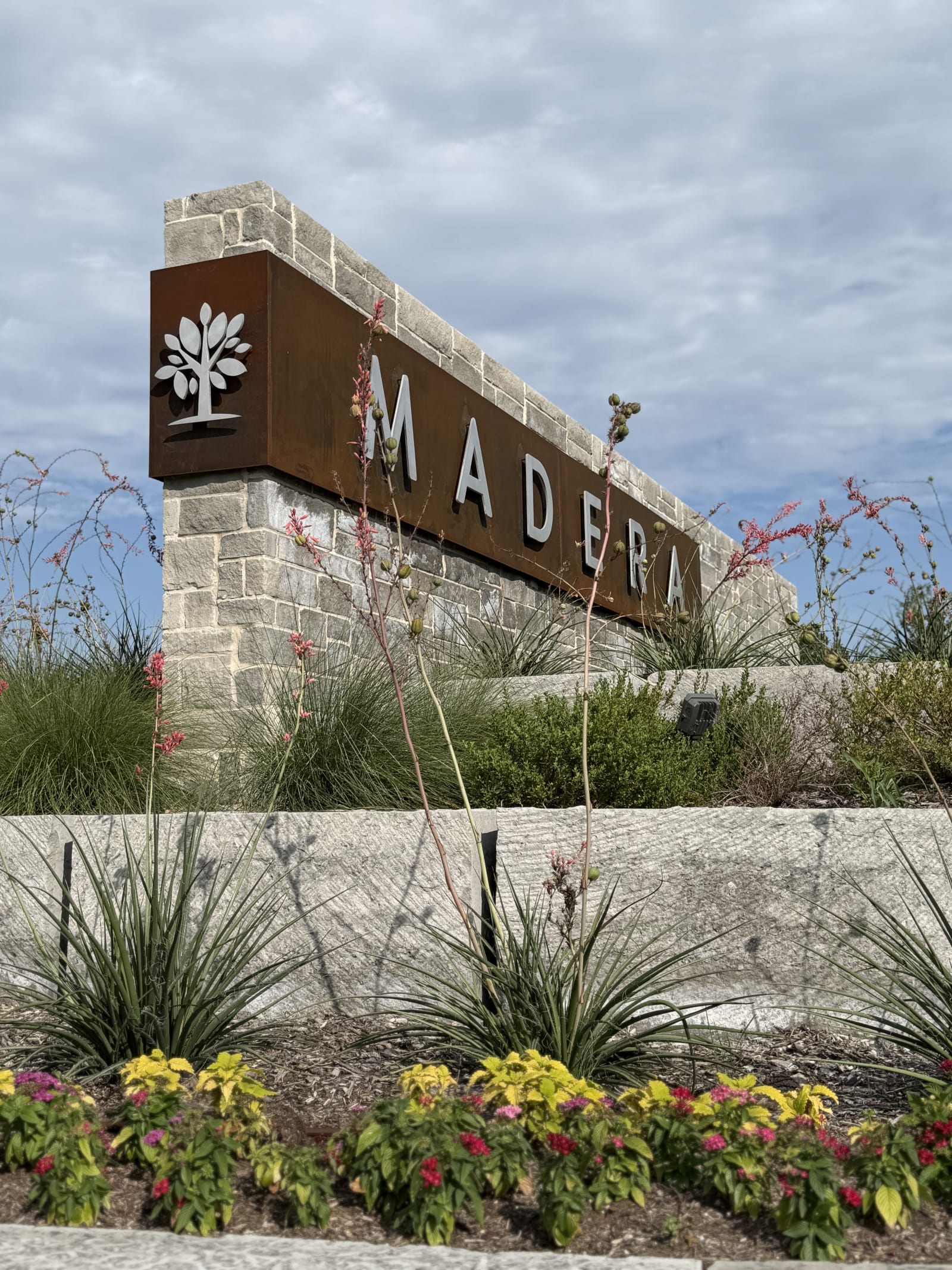Side view of the Madera entry monument showing stone masonry and steel signage in Royse City, TX