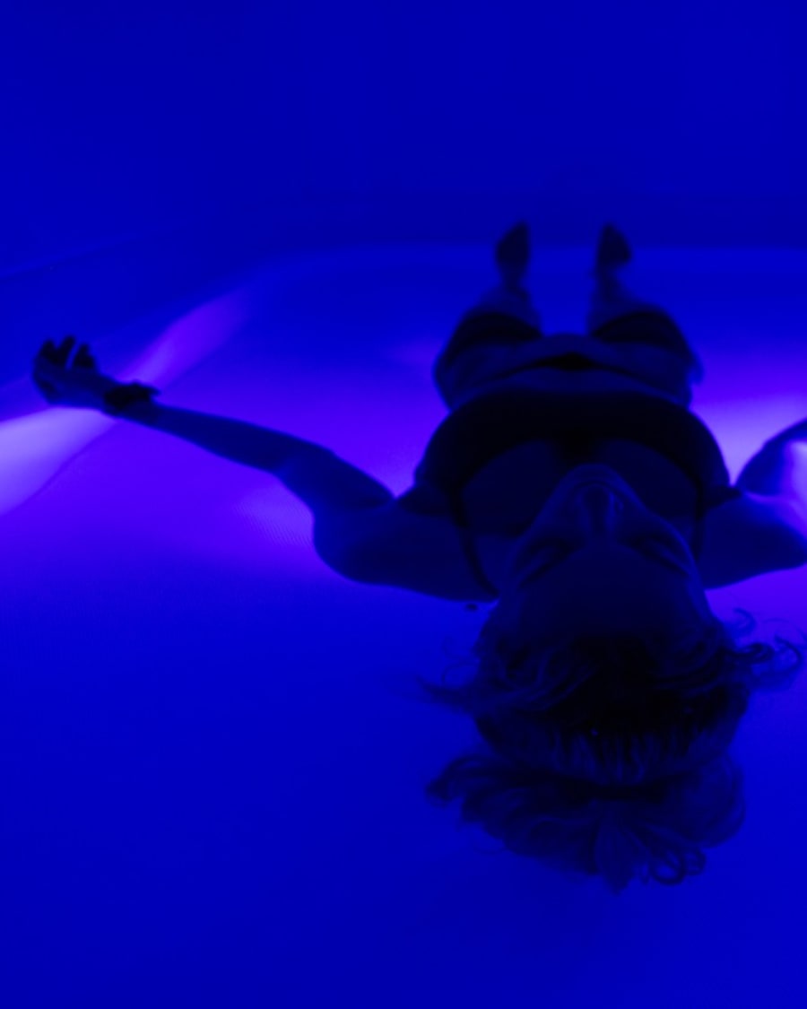 Guest floating on her back in the blue-lit float pod