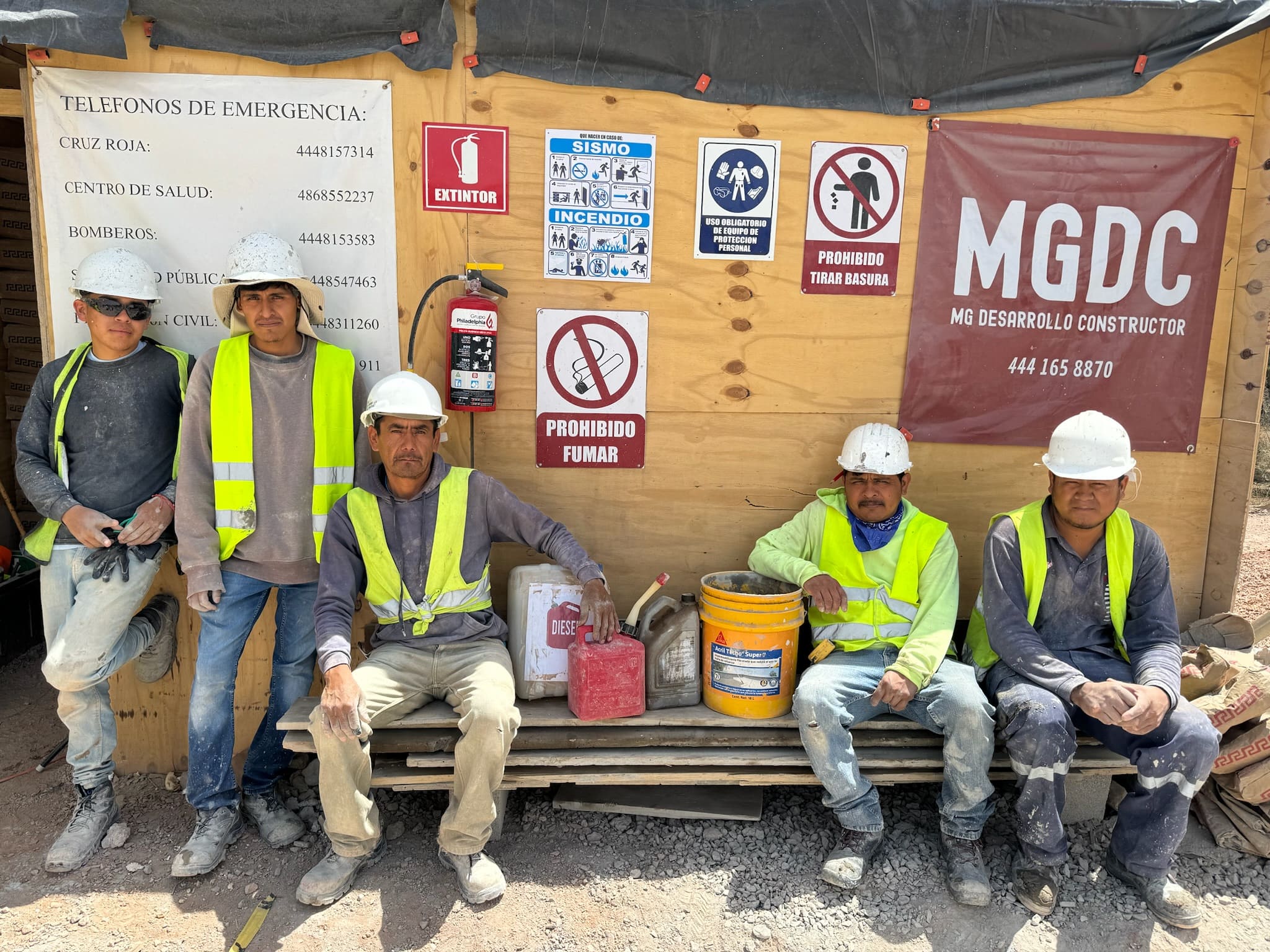 Equipo de construcción descansando junto a bodega de materiales con señalética de seguridad.