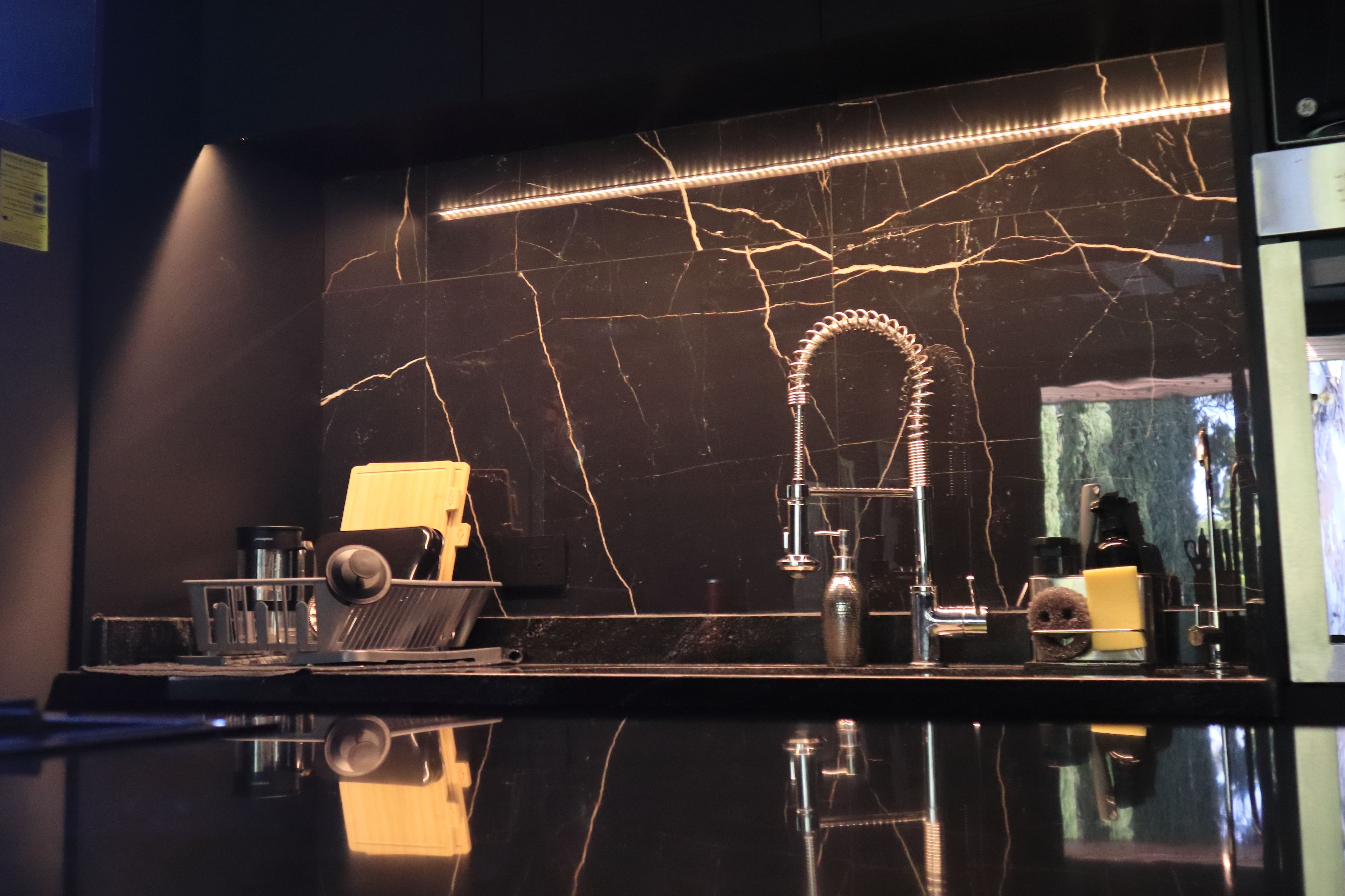 Acercamiento a la cocineta de Casa DRM, destacando el backsplash de mármol negro veteado y la iluminación LED indirecta que realza la estética oscura y la calidad de los materiales. Proyecto de MGDC en Campestre, SLP.