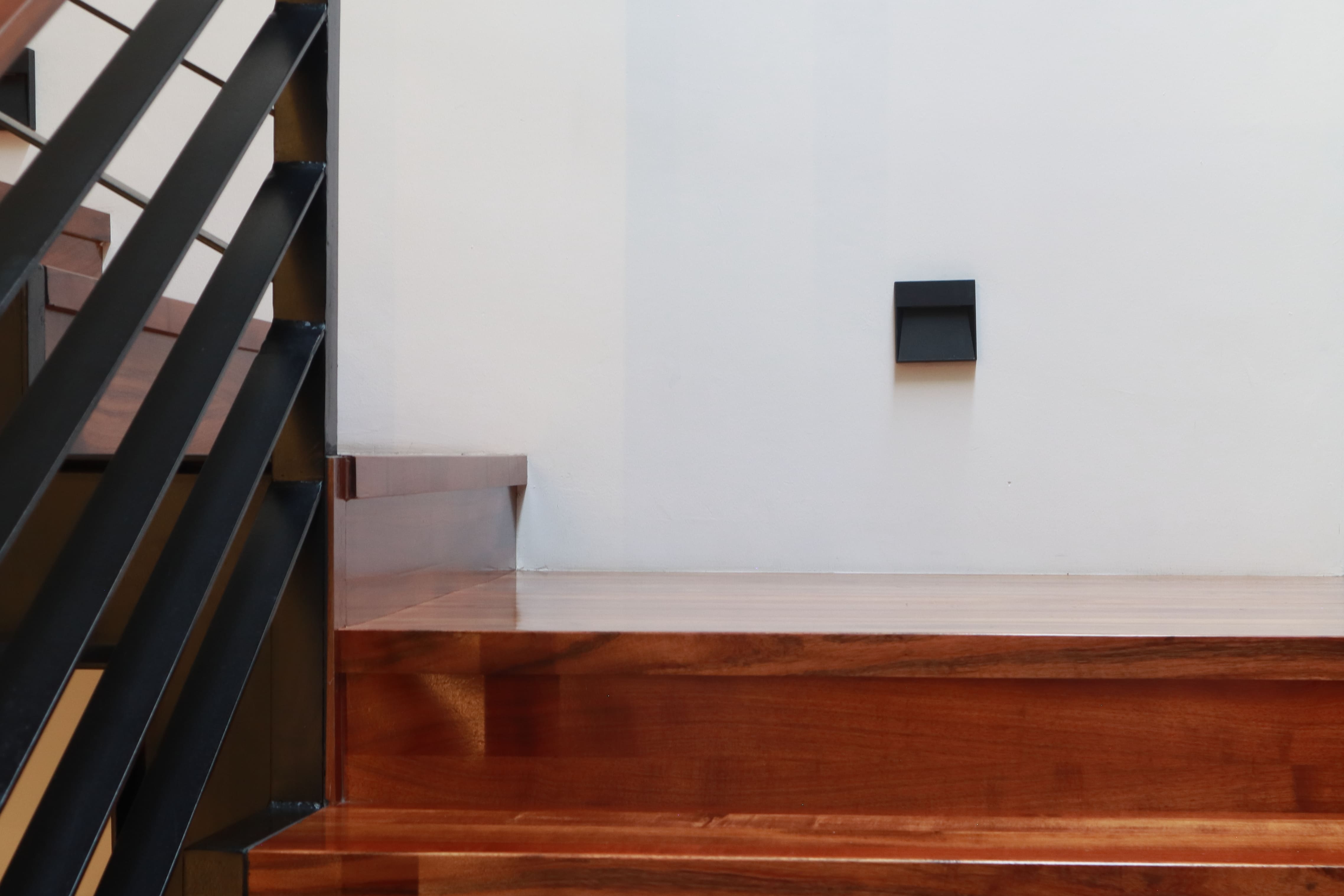 Detalle de los acabados de lujo en las escaleras de Casa DRM, mostrando la calidez de los escalones de madera en contraste con el barandal de herrería negro mate. Proyecto de MGDC en Campestre, SLP.