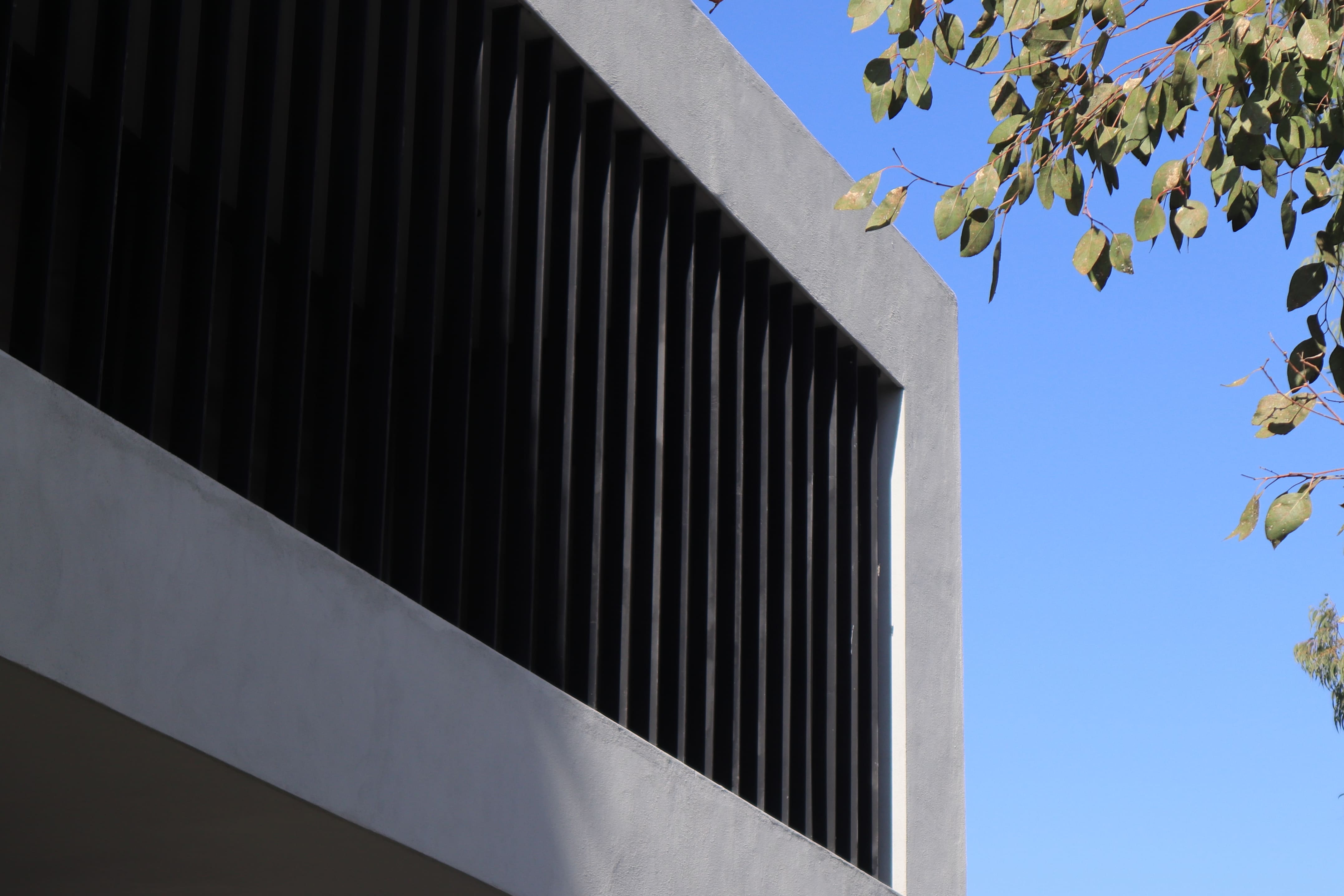 Detalle de la celosía arquitectónica y acabados grises de la fachada de Casa DRM bajo cielo azul, proyecto de MGDC en San Luis Potosí.