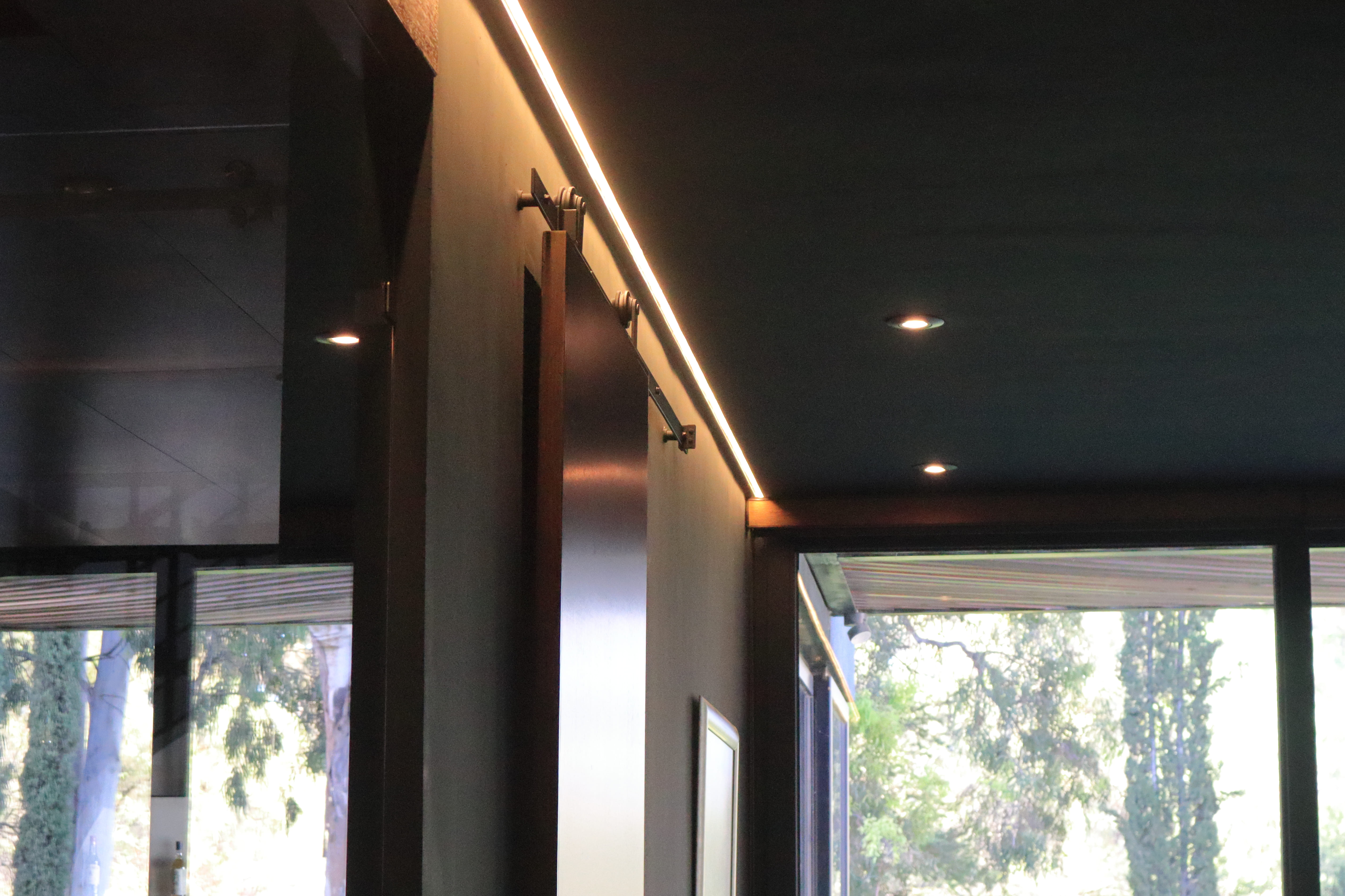 Detalle del diseño de iluminación en la sala-comedor de Casa DRM, destacando una tira de luz LED cálida indirecta instalada en el plafón oscuro. Proyecto de MGDC en Campestre, SLP.