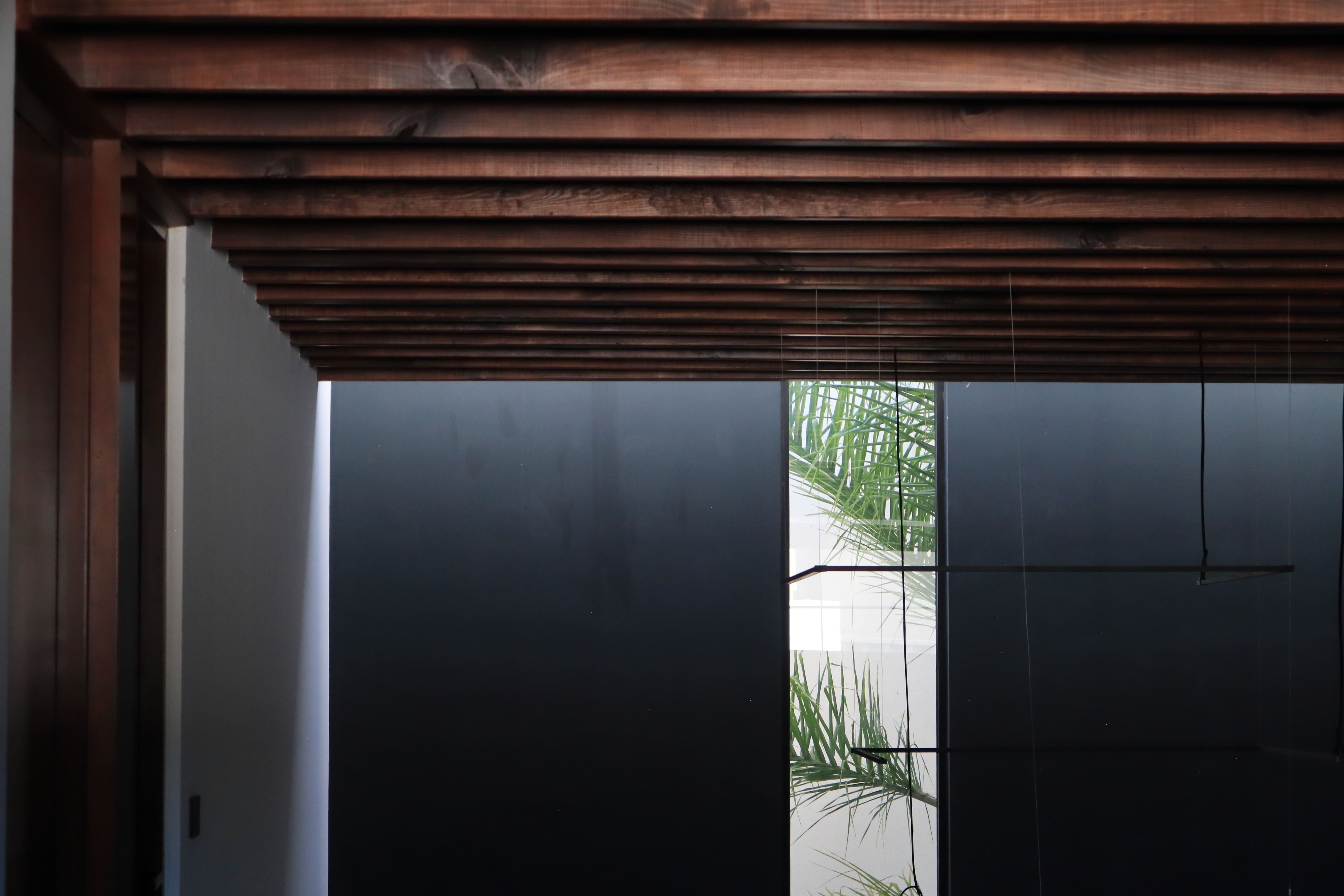 Detalle del plafón de madera natural tipo alfajía sobre el descanso de las escaleras en Casa DRM, con vista a un patio interior con palmeras. Diseño de interiores por MGDC en Campestre, SLP.