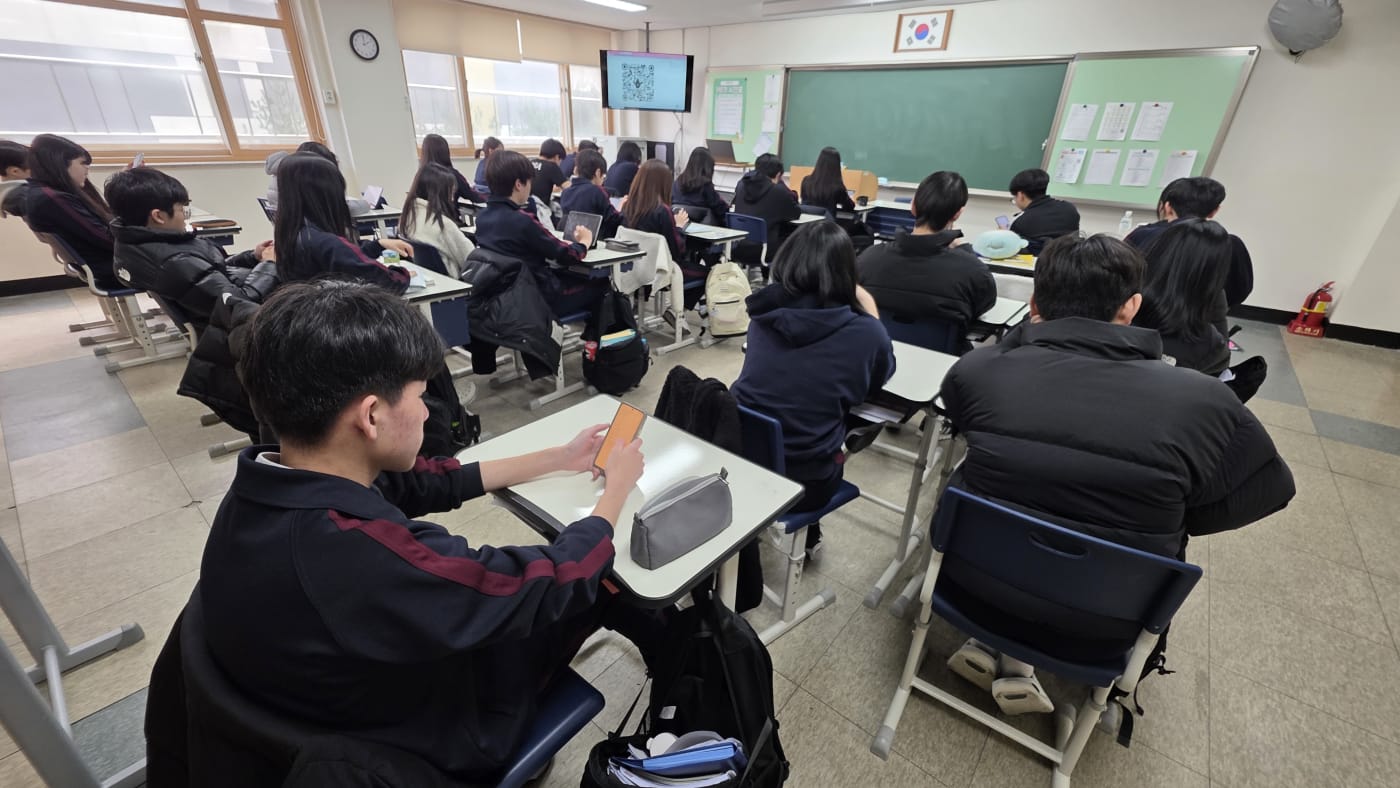 학생들이 태블릿과 스마트폰을 활용해 생성형 AI 학습에 몰두하고 있는 교실 전경입니다.