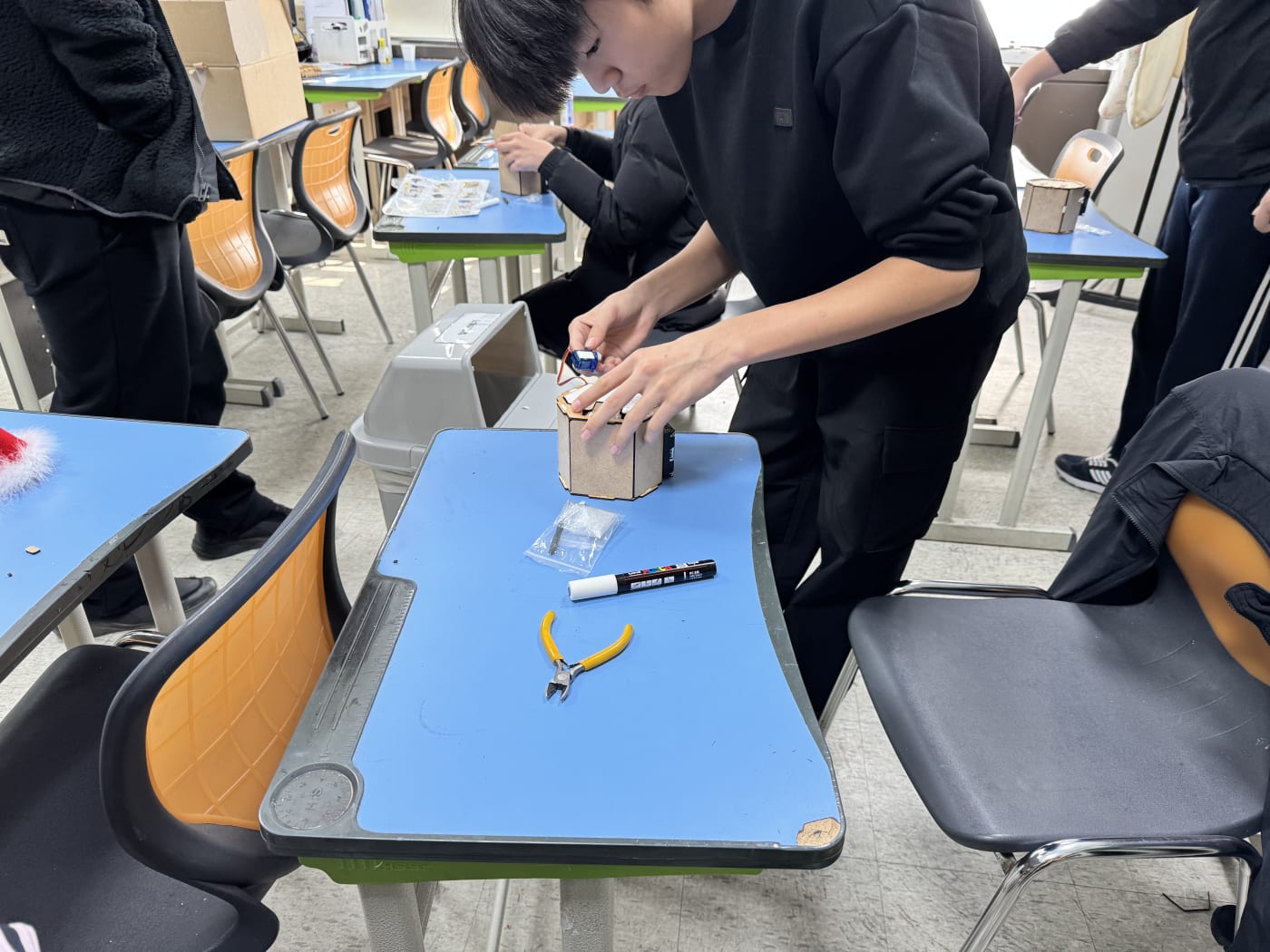 한 학생이 자리에서 일어나 로봇 휴지통의 최종 조립에 열중하고 있다.