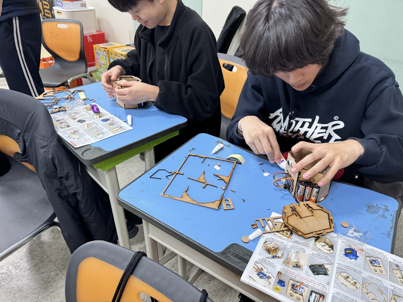 학생들이 진지한 표정으로 로봇 휴지통의 나무 프레임을 조립하고 있다.