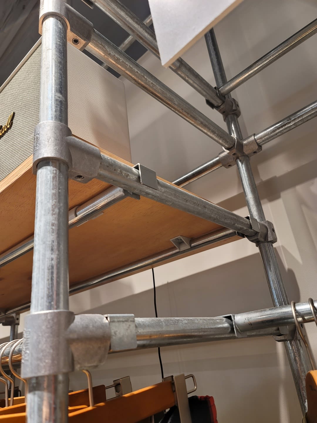 금속 파이프와 선반이 정교하게 결합된 집기 디테일 이미지입니다. 매끄러운 알루미늄 피팅과 스틸 파이프의 질감이 어우러져 현대적이고 전문적인 느낌을 주는 전시 구조물의 일부분을 보여줍니다.