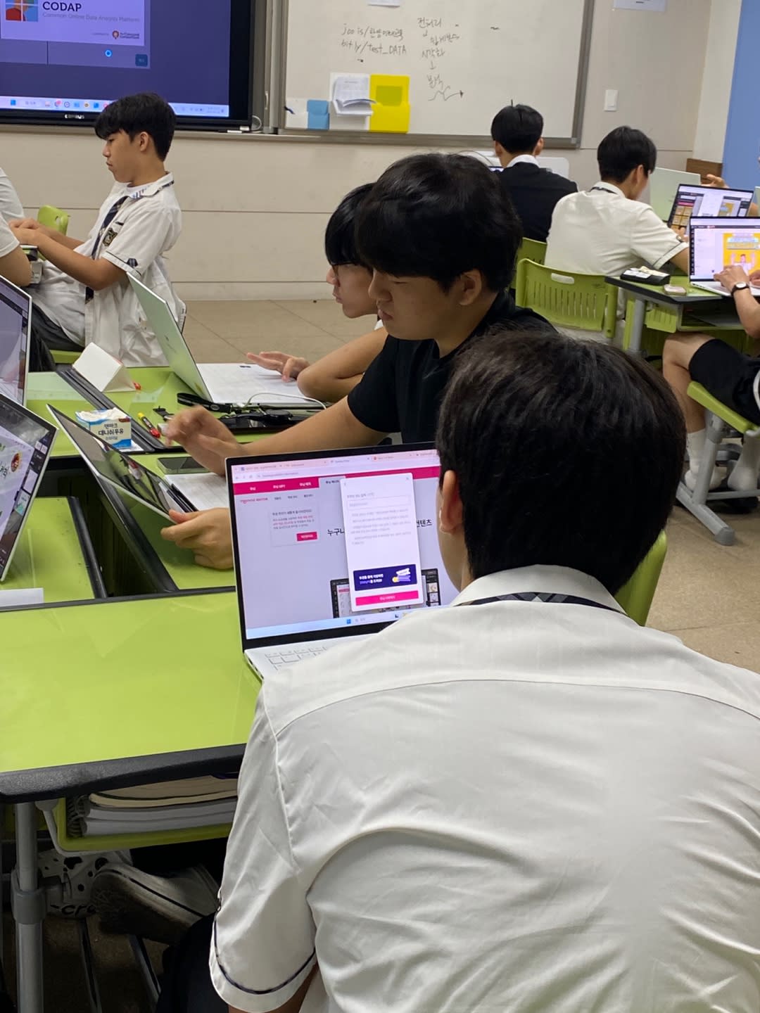디지털 플랫폼이 띄워진 노트북을 활용해 인공지능의 원리나 데이터 분석을 학습하는 학생들의 뒷모습과 열기 가득한 강의실 풍경입니다.