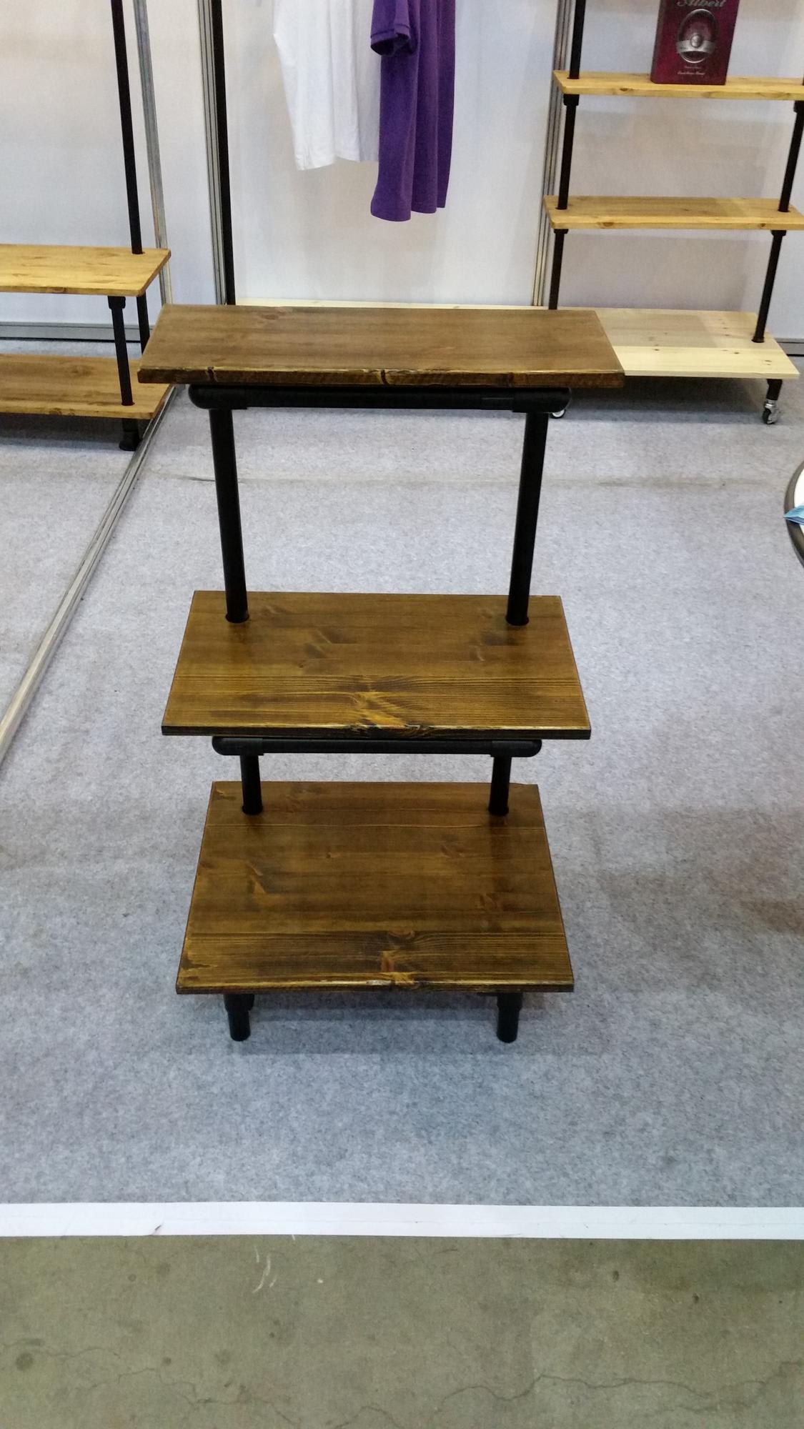 원목의 따뜻한 질감과 매트한 블랙 파이프가 조화를 이루는 3단 이동식 진열 가구입니다. 하단 바퀴를 통해 공간 활용도를 높인 리테일 매장용 모듈러 디자인의 정석을 보여줍니다.