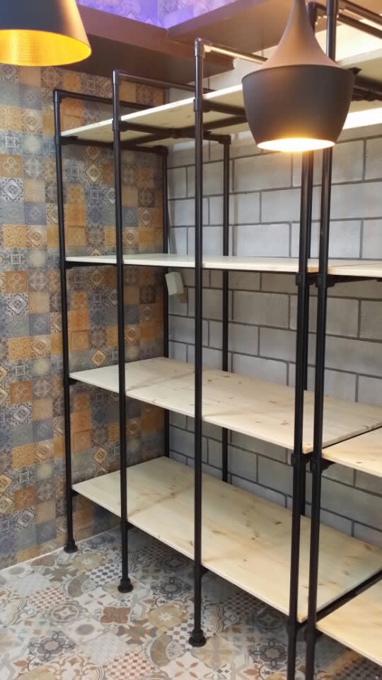 벽면을 가득 채운 인더스트리얼 스타일의 대형 선반 시스템입니다. 밝은 톤의 목재 상판과 수직으로 뻗은 블랙 파이프가 대비를 이루어 공간에 웅장함과 정돈된 무드를 선사합니다.