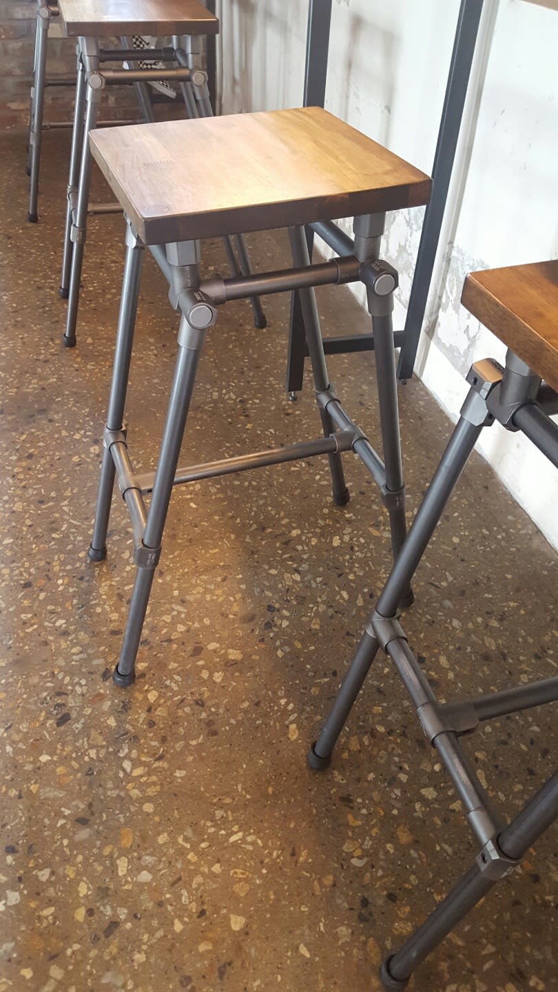 거친 질감의 바닥과 조화를 이루는 메탈 파이프 프레임의 바 스툴입니다. 용접 없이 견고하게 체결된 조인트 디테일이 인더스트리얼 카페 특유의 날것 그대로의 매력을 극대화합니다.