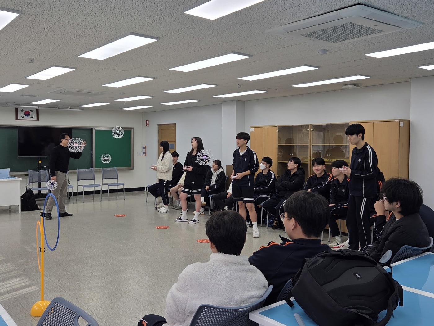 학생들이 직접 드론을 조종하며 장애물을 통과시키는 실습 장면입니다. 손에 땀을 쥐게 하는 긴장감과 재미가 공존하는 활동적인 분위기입니다.