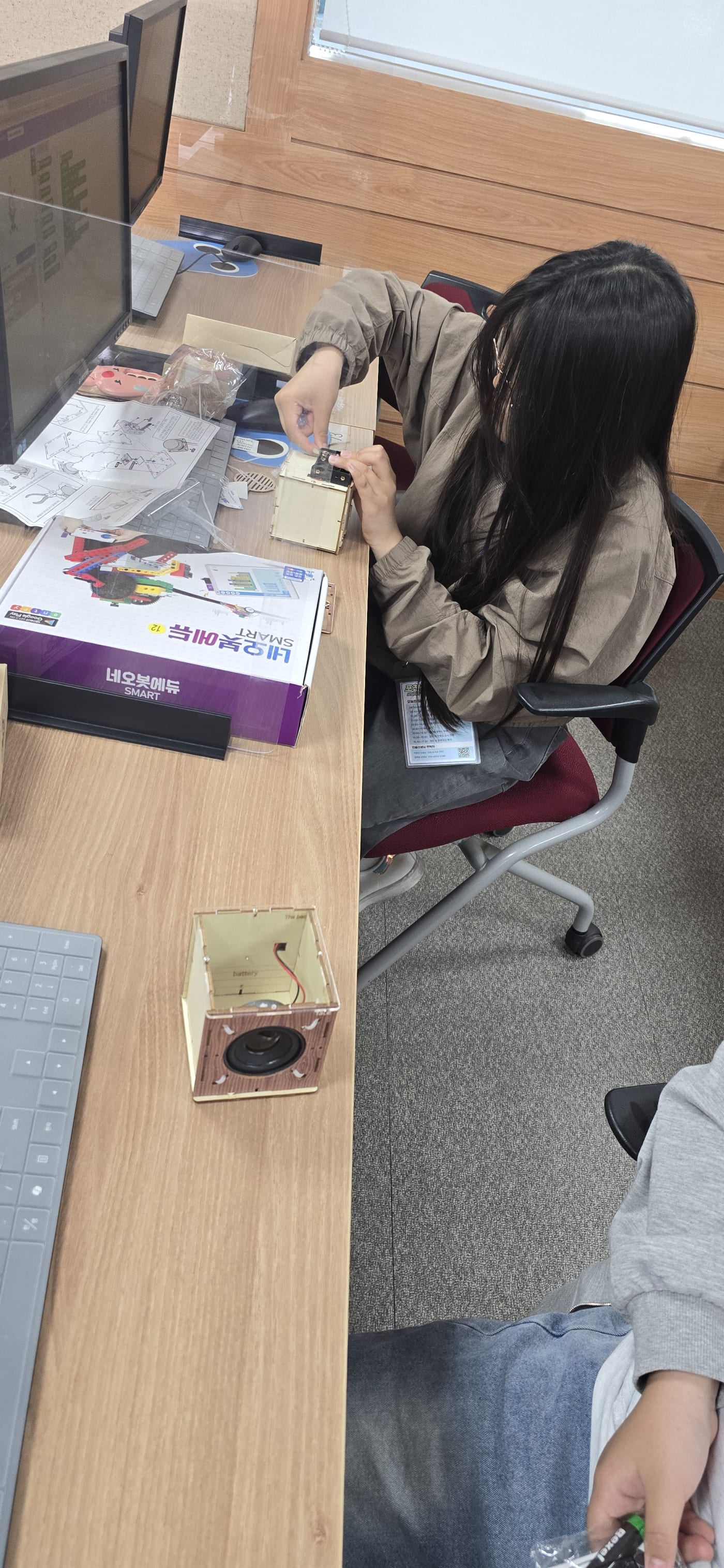 목재 프레임을 사용하여 자신만의 블루투스 스피커를 완성해 나가는 학생의 섬세한 조립 과정입니다.