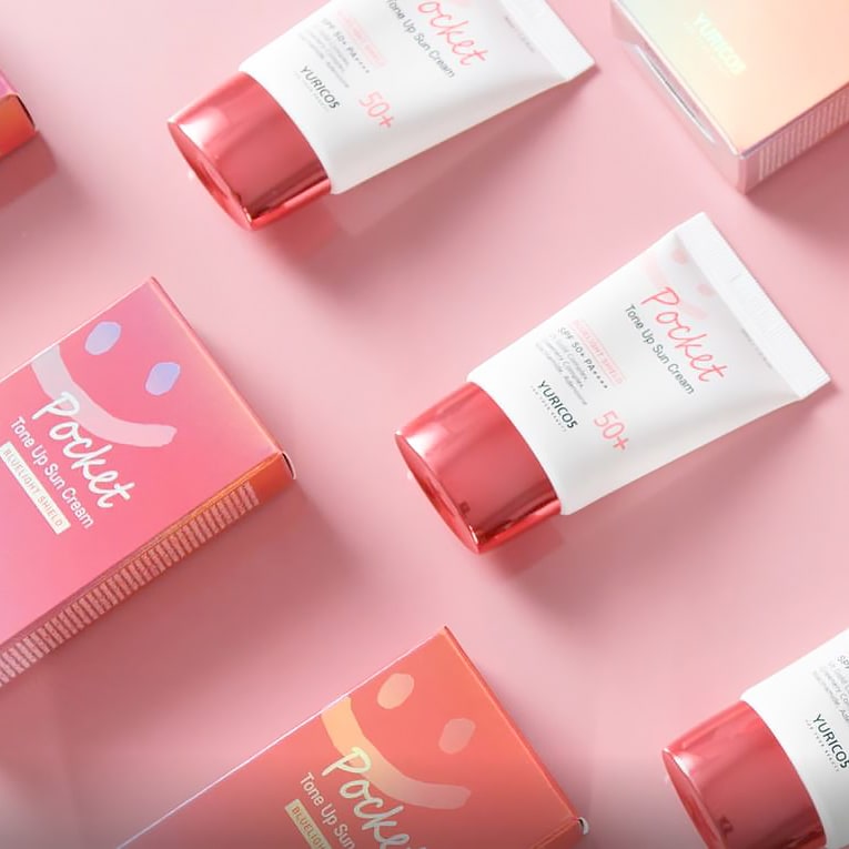 Array of YURICO5 Pocket Tone-Up Sunscreens on a bright pink theme. They boast affordable pricing, portability, and stylish package design.