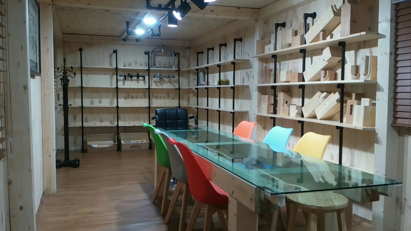 블랙 파이프 피팅을 사용하여 벽면 전체 선반과 대형 유리 상판 테이블의 하부 프레임을 제작한 세련된 사무 및 워크숍 공간입니다.