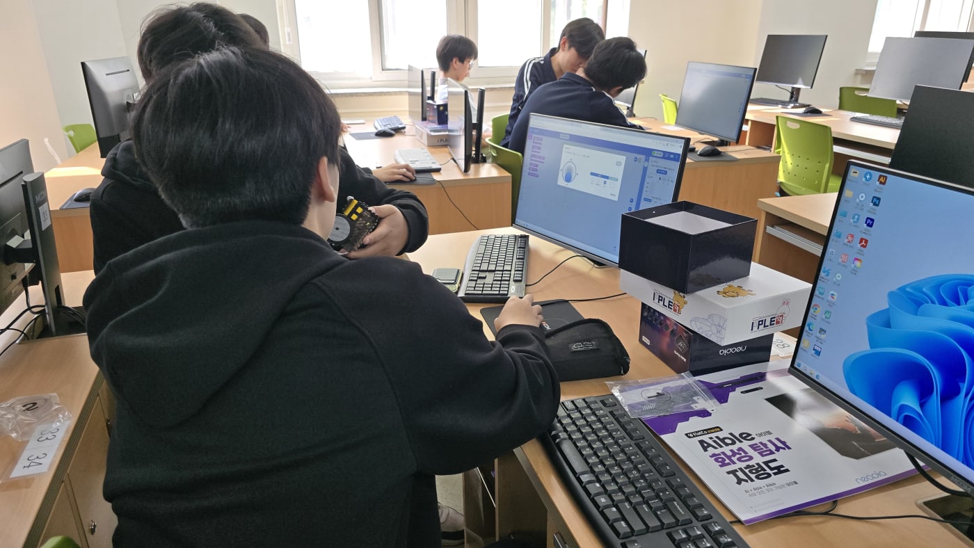 코딩 화면과 실제 로봇을 번갈아 보며 이론과 실무를 연결하는 학생의 진지한 모습