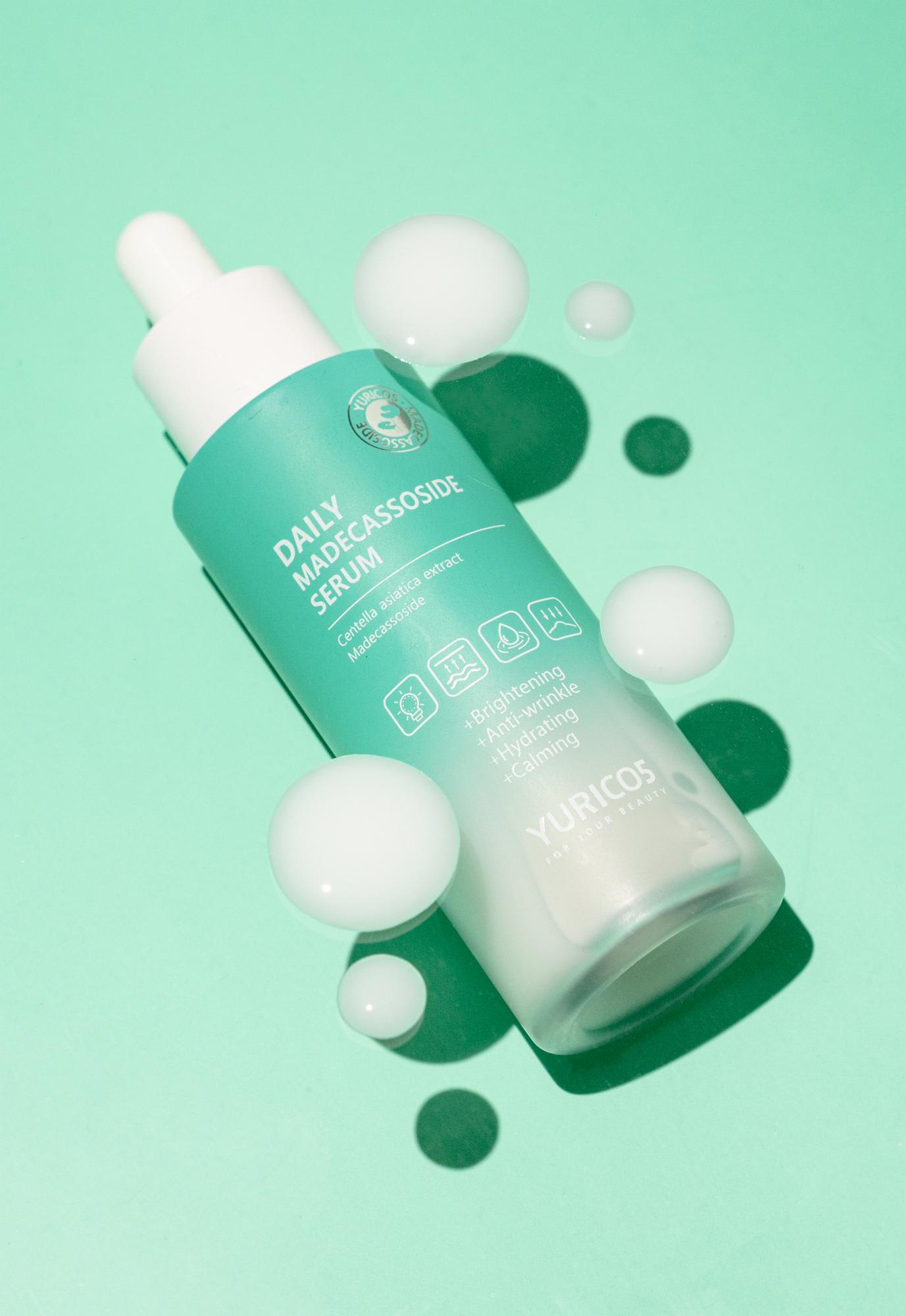 Mint green bottle with drops of moisture elegantly complementing YURICO5's 'Daily Madecassoside Serum'. It visibly showcases features of the soothing and moisturizing formula.
