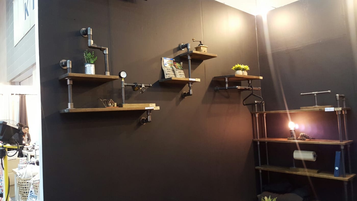블랙 월에 설치된 파이프 선반 시스템으로 인더스트리얼 인테리어 무드를 연출했습니다. 목재 선반과 파이프 라인이 조화롭게 어우러져 세련된 수납 공간과 소품 배치를 돋보이게 합니다.