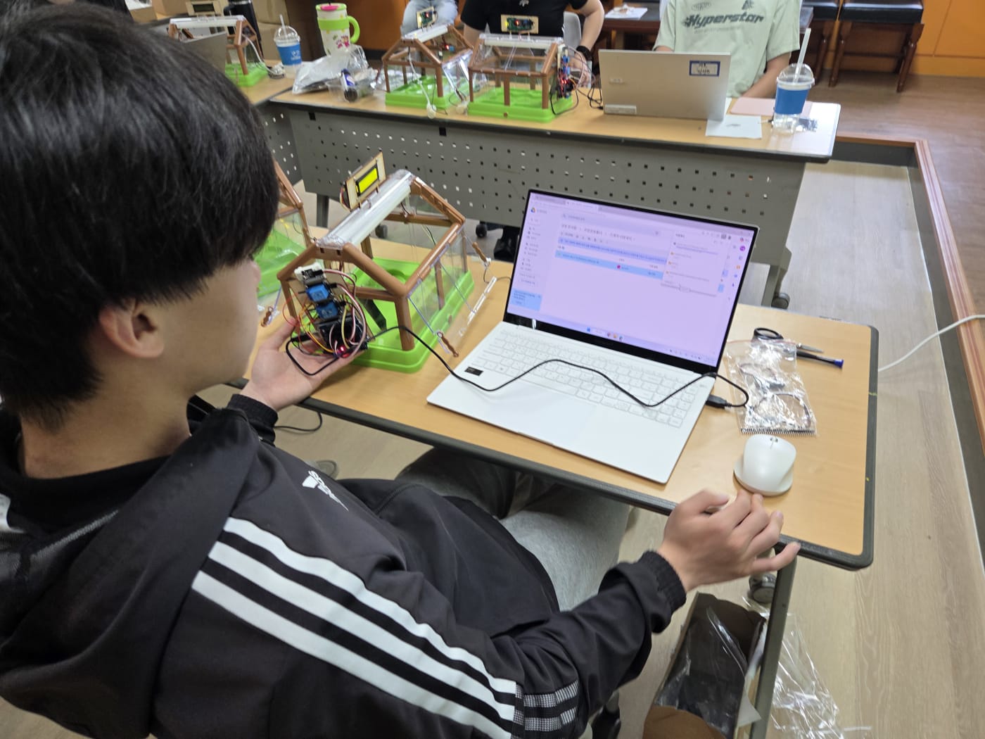 노트북으로 코딩 소스를 확인하며 스마트팜 기기를 조작하는 모습으로, 디지털 리터러시 교육의 핵심을 보여줍니다.