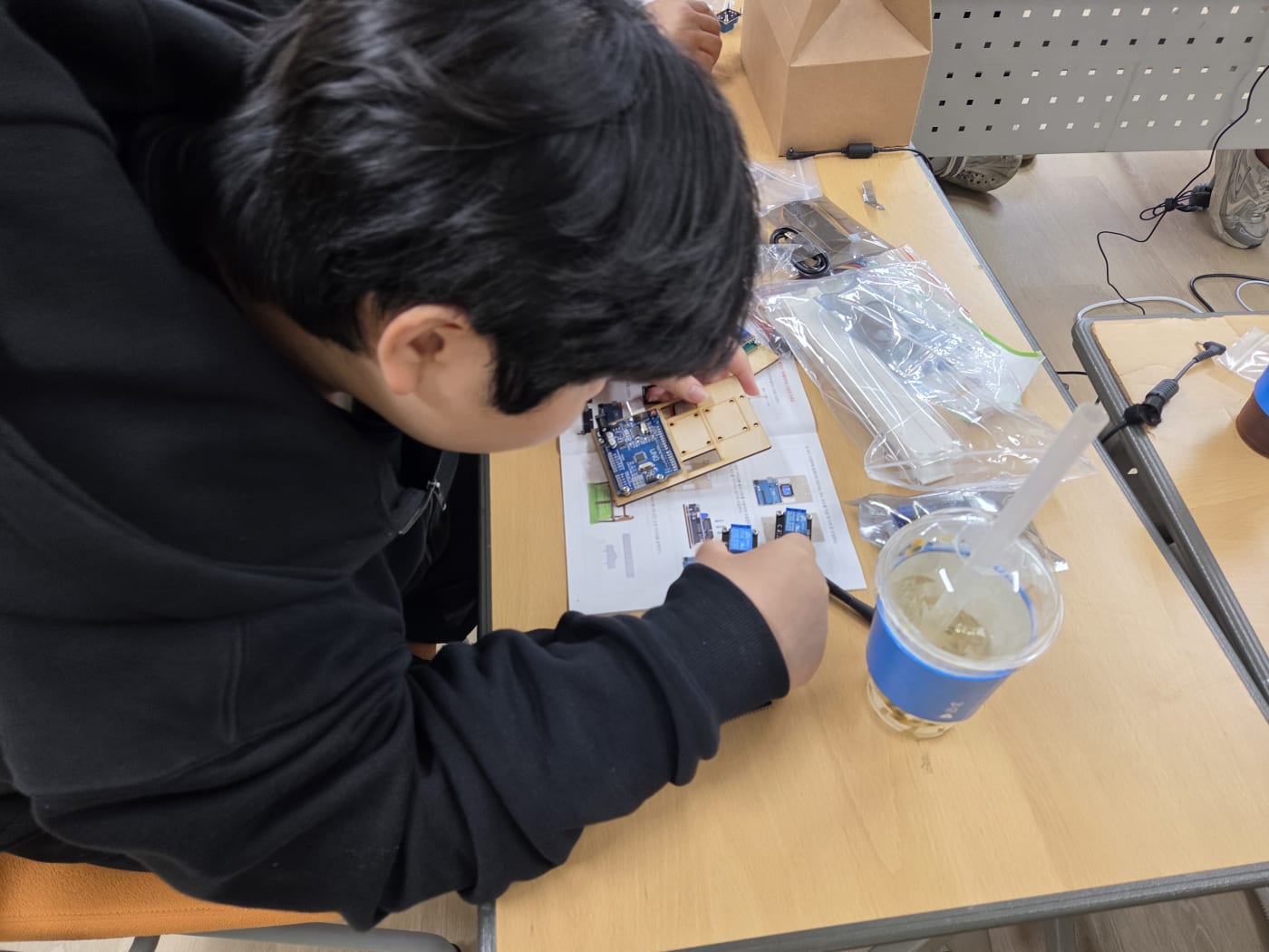 설계도를 보며 아두이노 보드와 부품을 조립하는 손길을 근접 촬영하여 체계적인 DIY 교육 과정을 보여줍니다.