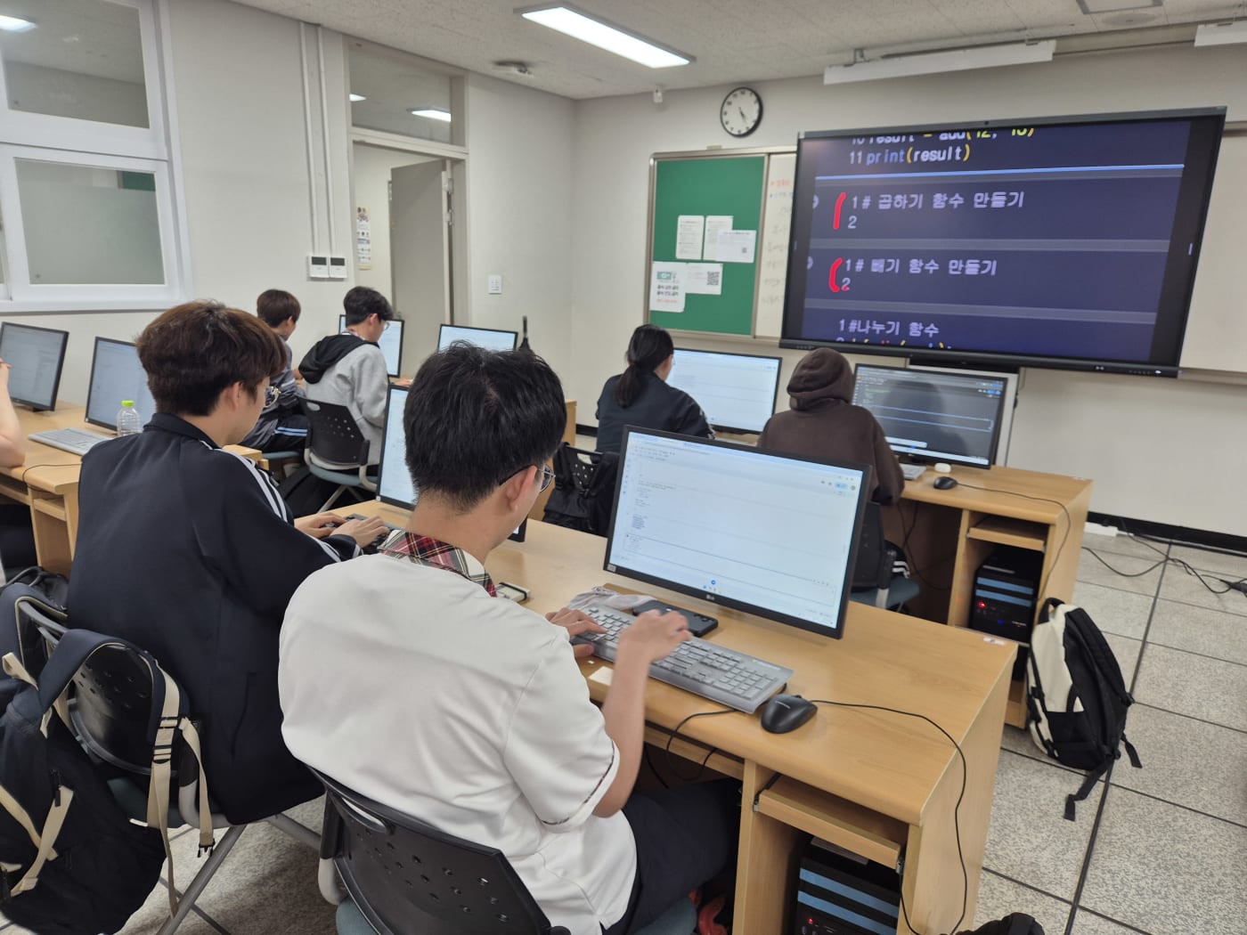 학생들이 각자의 모니터에서 파이썬 함수 정의와 결과 출력 실습에 몰두하고 있는 장면입니다.
