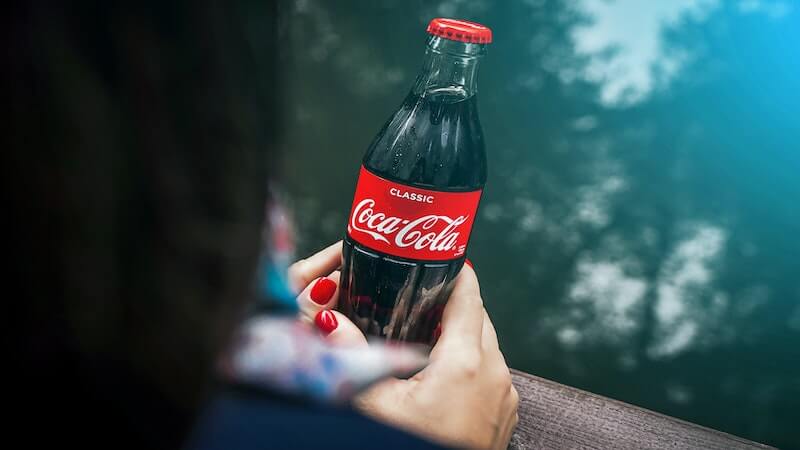 The image shows a woman holding a bottle of Coke