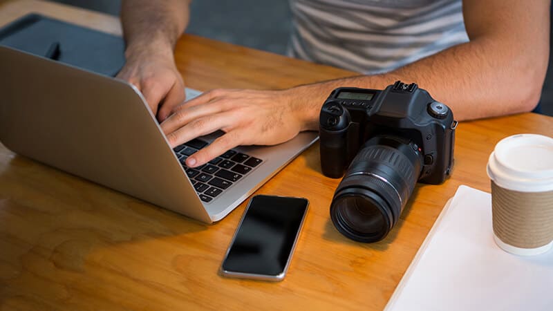 Foto de uma pessoa mexendo em um notebook em cima da mesa com câmeras