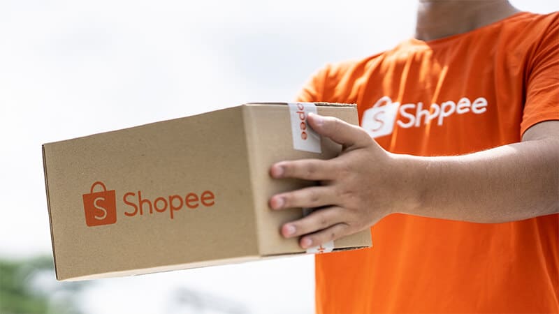 Foto de uma pessoa com a camisa da Shopee segurando uma caixa da Shopee