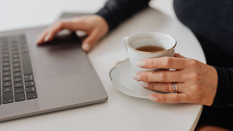 Foto de uma pessoa usando um notebook e segurando uma caneca com café