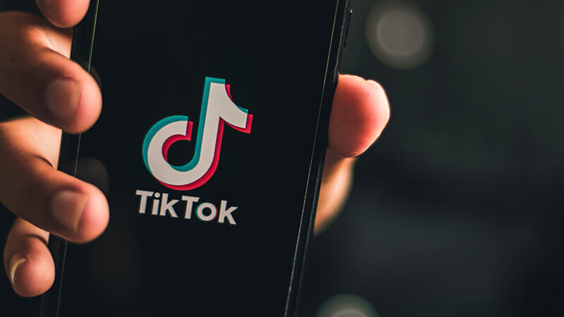 Foto de uma pessoa segurando um celular com o logo do TikTok