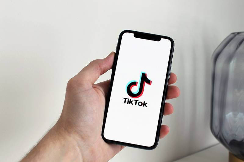 The image shows a person holding a smartphone. TikTok's logo appears in the smartphone screen.