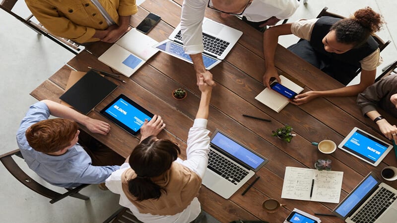 Foto de uma mesa com várias pessoas e notebooks