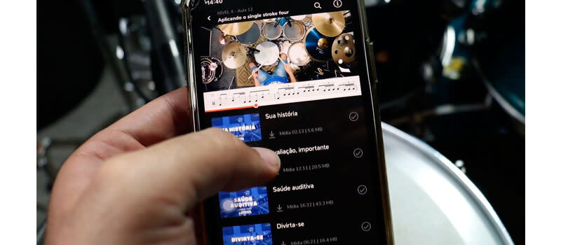 Instrutor mostrando a playlist de aulas do curso em seu celular enquanto está sentado em sua bateria