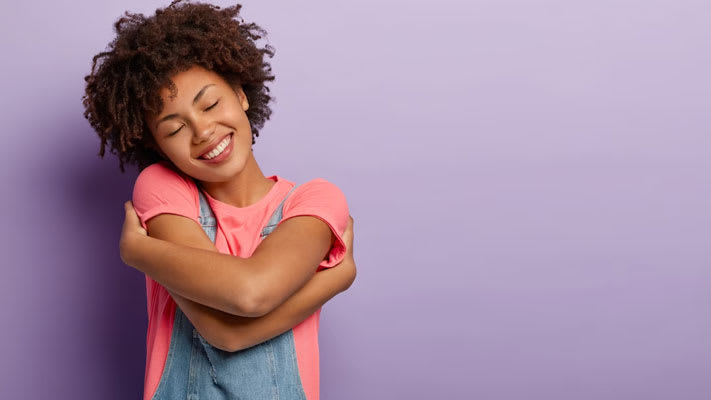 Foto de una mujer que se abraza con placer, siente comodidad, calma y amor, y sonríe