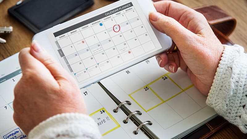 Imagem de uma mão segurando um celular aberto em um calendário