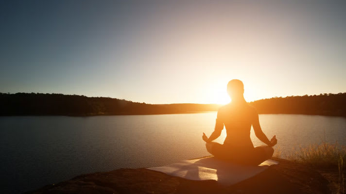 Foto de una mujer meditando frente a un lago.