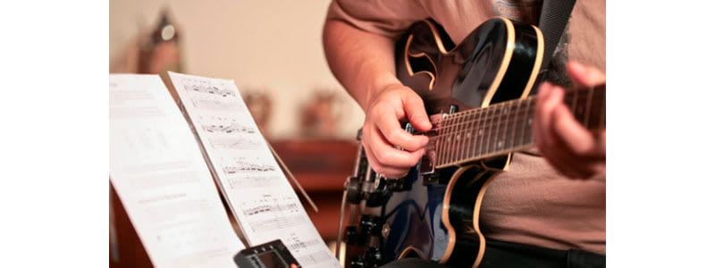 aluno tocando guitarra enquanto lê uma tablatura