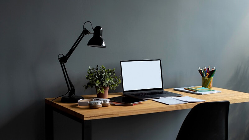 imagem que mostra uma mesa, uma cadeira e uma estante em uma sala com parede branca