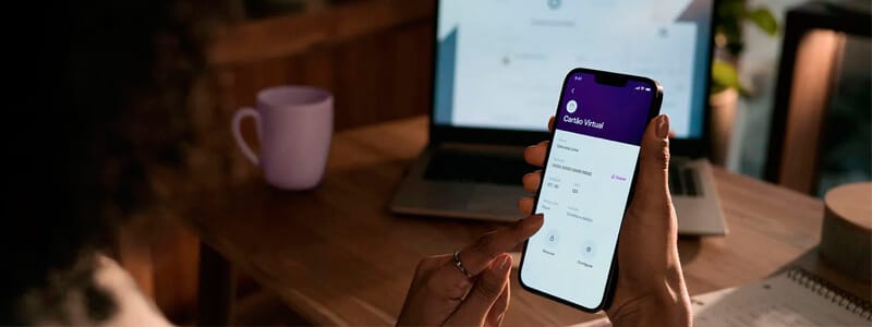 pessoa sentada em frente a mesa usando o app do nubank e seu cartão virtual