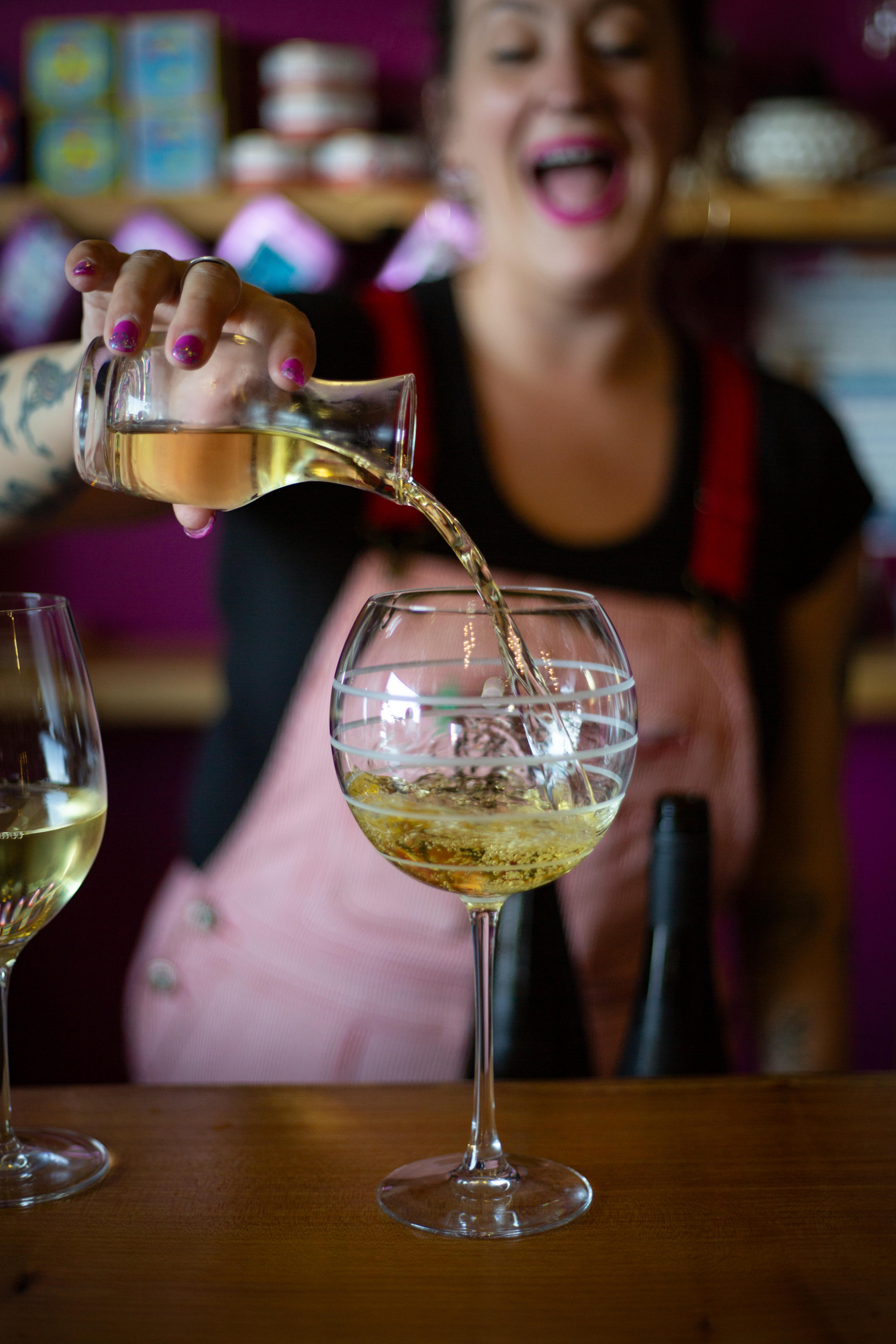 Woman pouring golden wine from bottle into glass with shelves of wine bottles in background