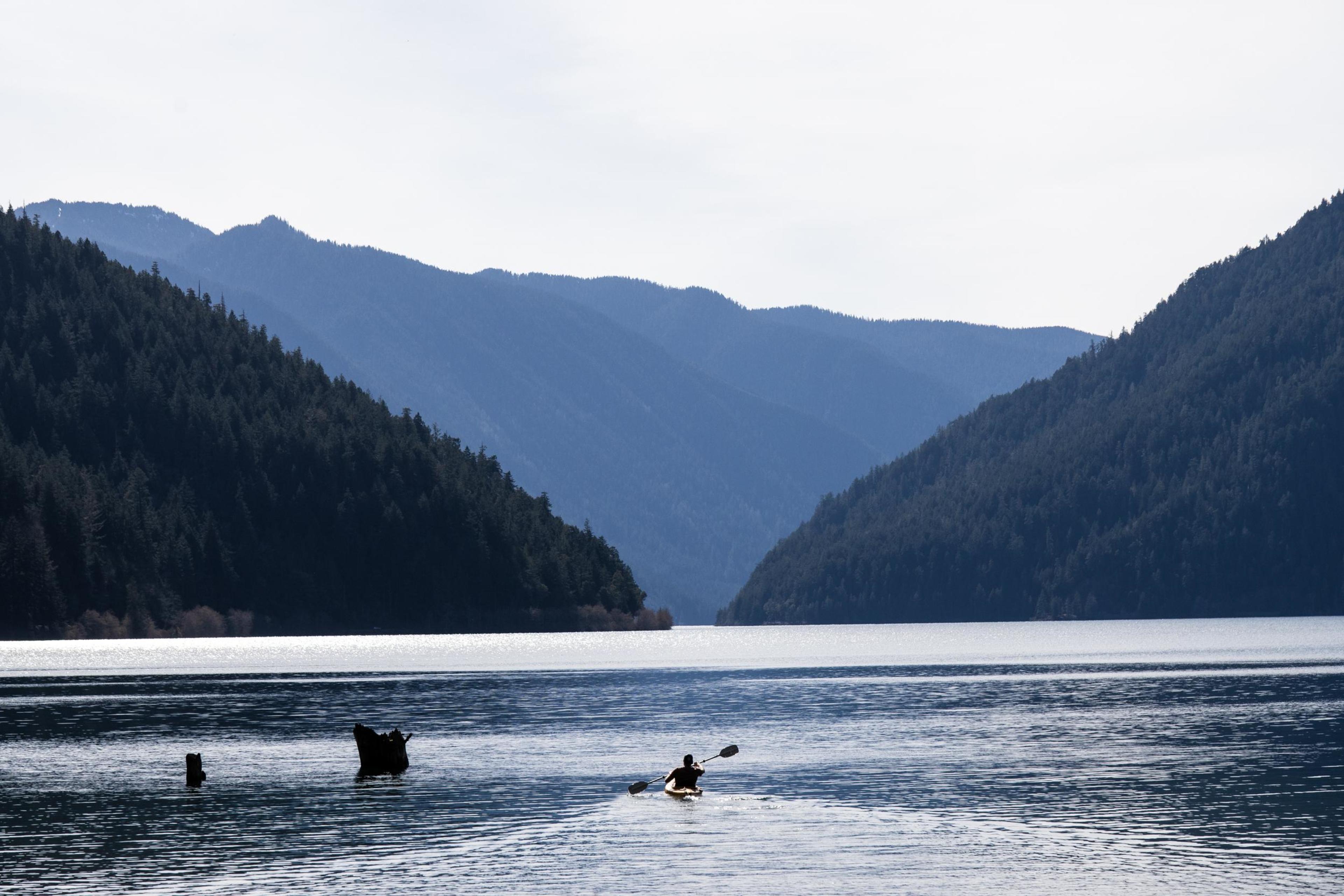 Kayaker paddling across Lake Crescent with forested mountains rising in the background