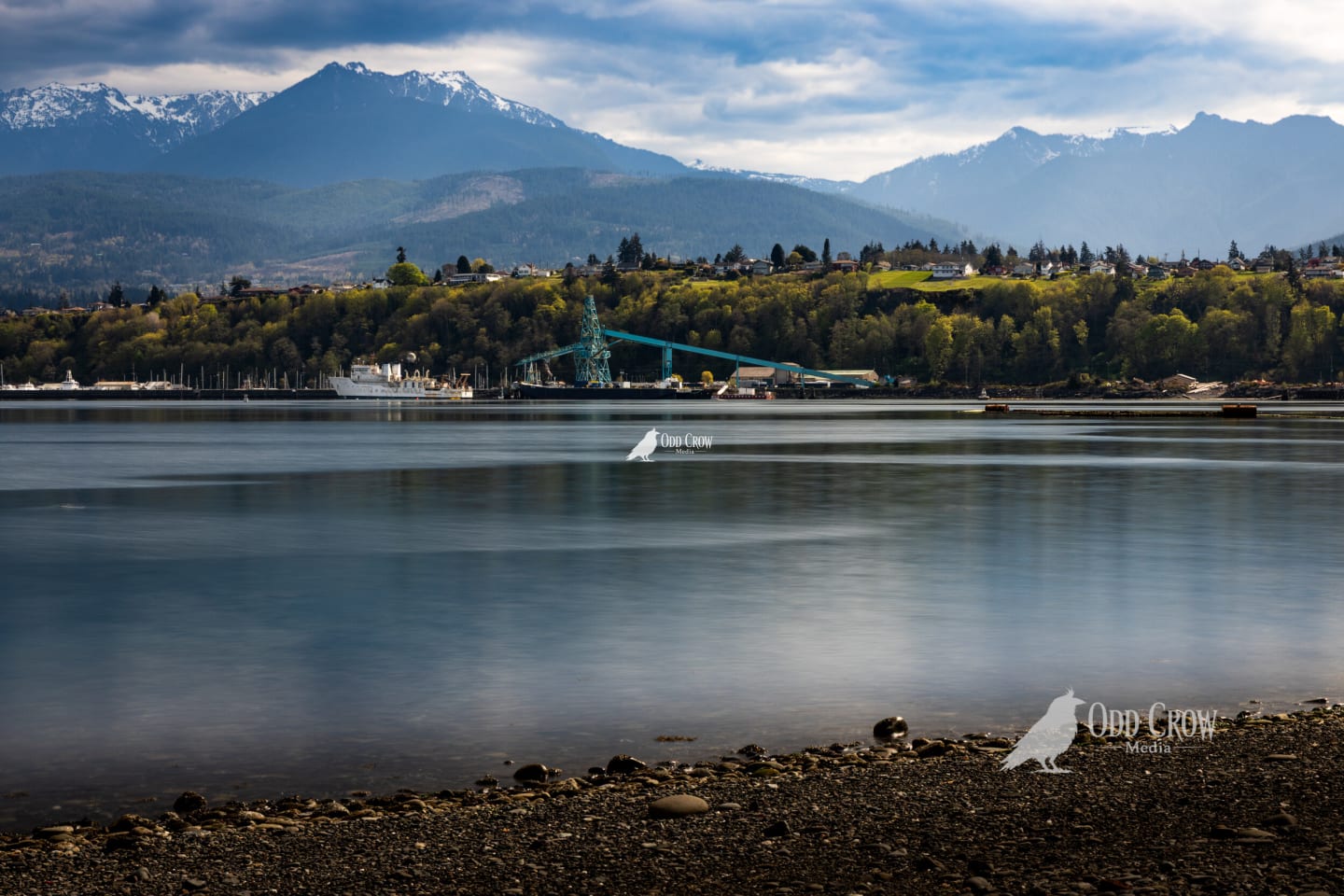 Serene harbor view with ultra-smooth water and snow-covered Olympic Mountains under dramatic cloudy sky