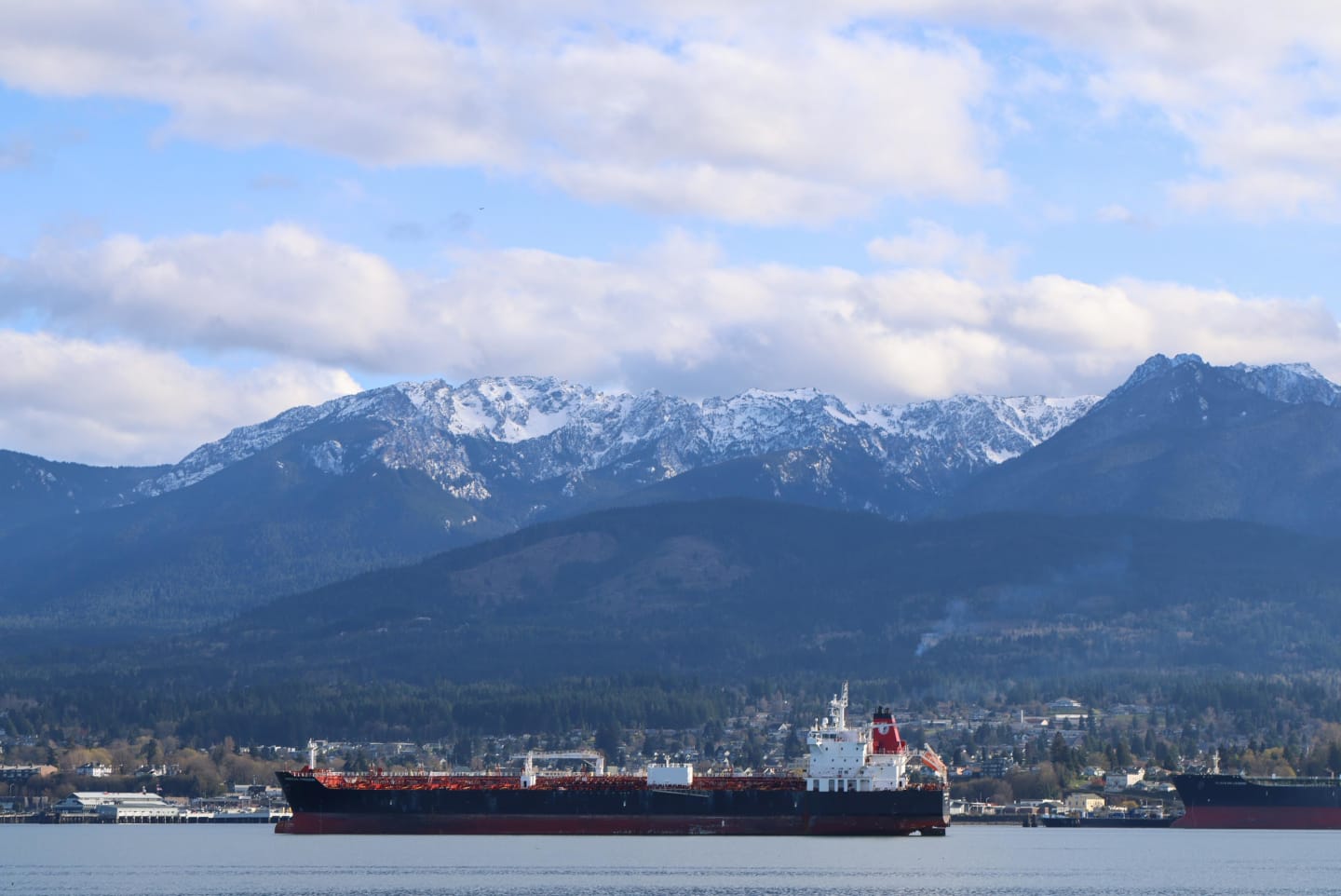 Large red tanker ship anchored in Port Angeles harbor with snow-covered Olympic Mountains in the background