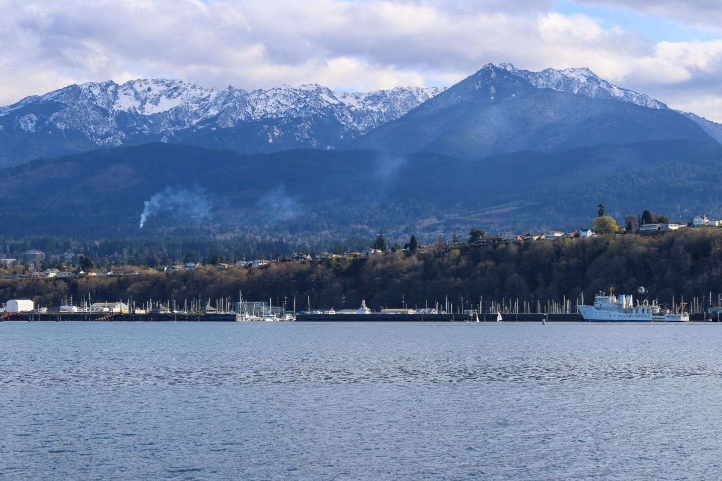 Port Angeles marina with various boats and vessels against backdrop of snow-covered Olympic Mountains